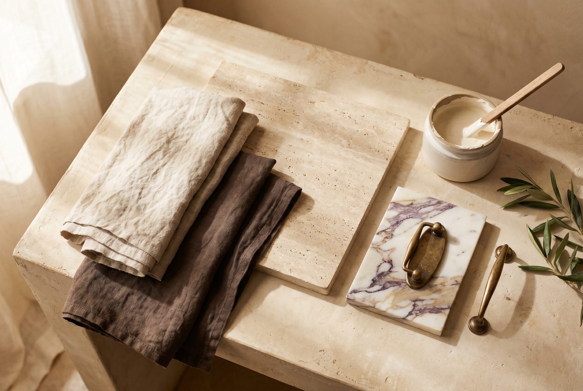 Material palette of linen swatches, travertine, marble, and brass hardware on plaster